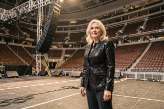 Femme artiste chevronnée en veste sequins noire au bord d'une immense scène de concert lors d'une répétition du Celebration Tour 2026